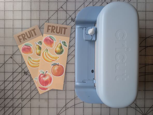 A blue Cricut Joy 2 beside two sheets of fruit stickers