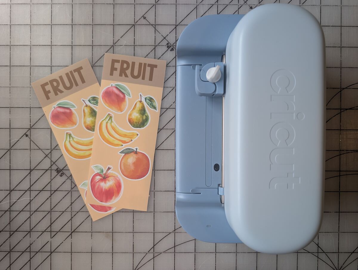 A blue Cricut Joy 2 beside two sheets of fruit stickers