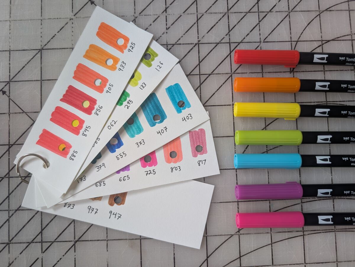 A rainbow of Tombow Dual Brush Pens laying beside a set of swatch cards