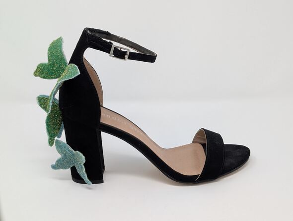 A black high heeled shoe with three blue and green sparkly butterflies glued to the back
