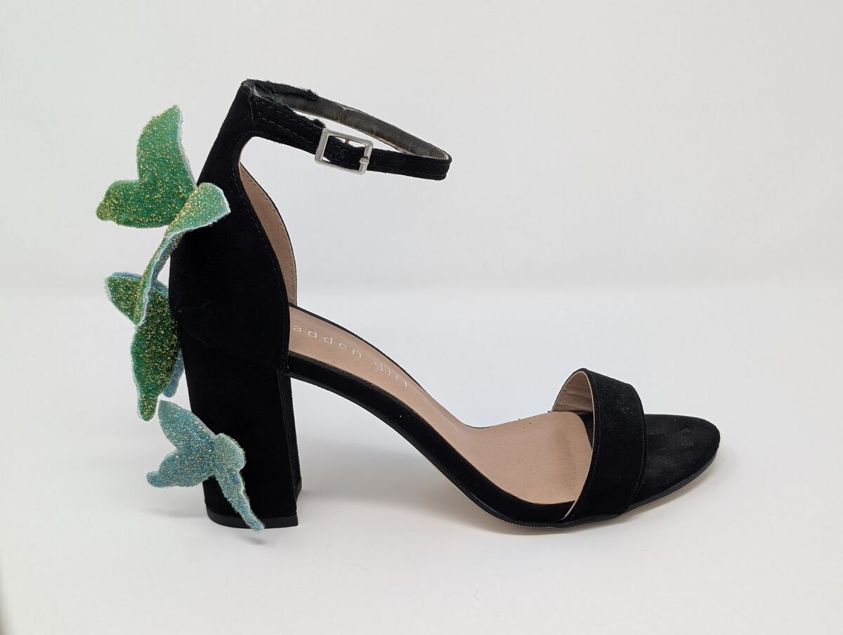 A black high heeled shoe with three blue and green sparkly butterflies glued to the back